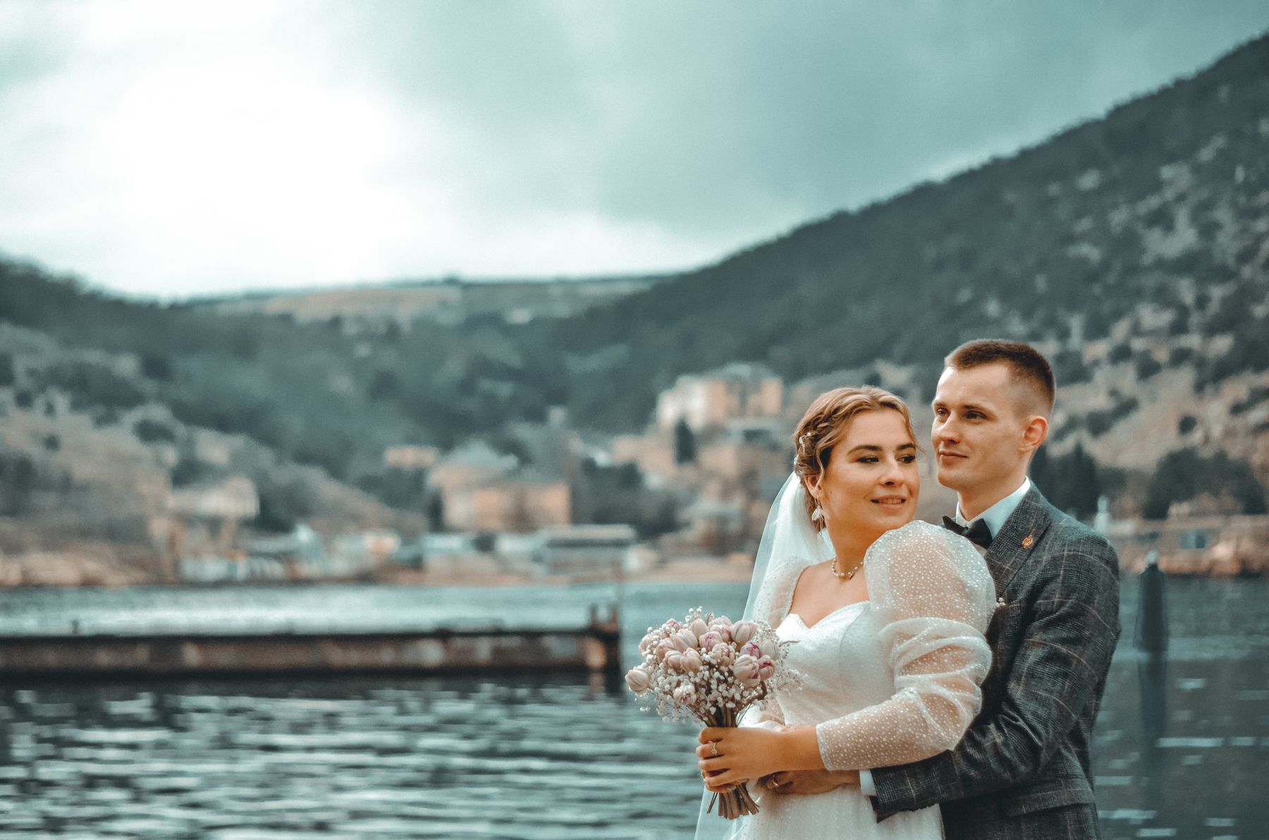 Dağlarla çevrili göl kıyısında, buket tutan gelin ve damat